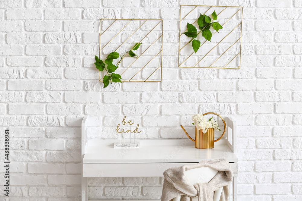 Modern workplace with vase and lilac flowers near brick wall