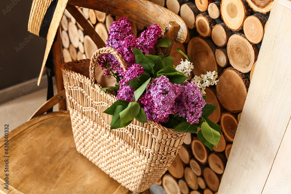 Bag with lilac flowers on chair near wooden wall