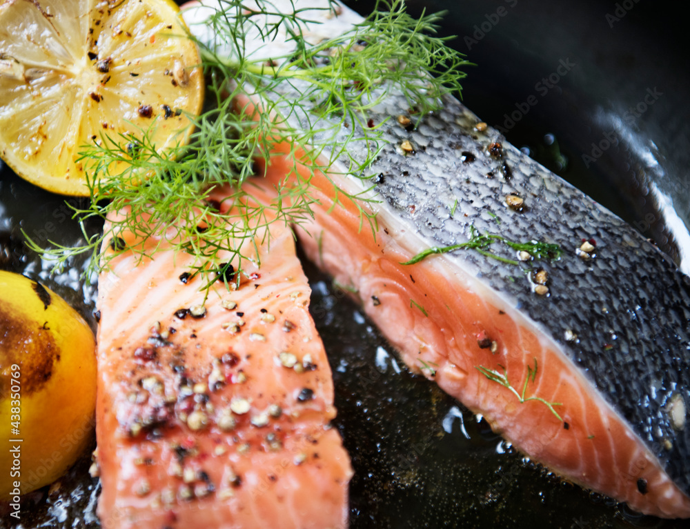 Grilled salmon fillet being sprinkled with salt and pepper