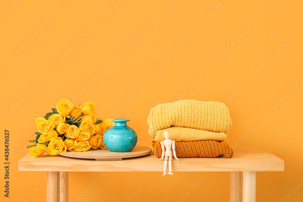 Beautiful yellow roses and clothes on table near color wall