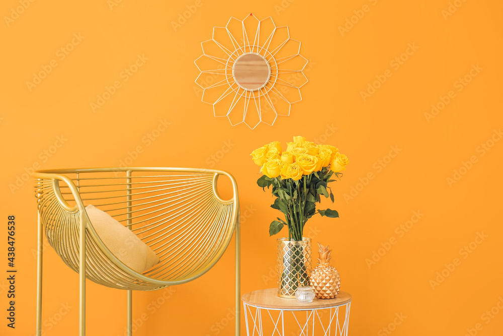 Vase with yellow roses on table and armchair near color wall