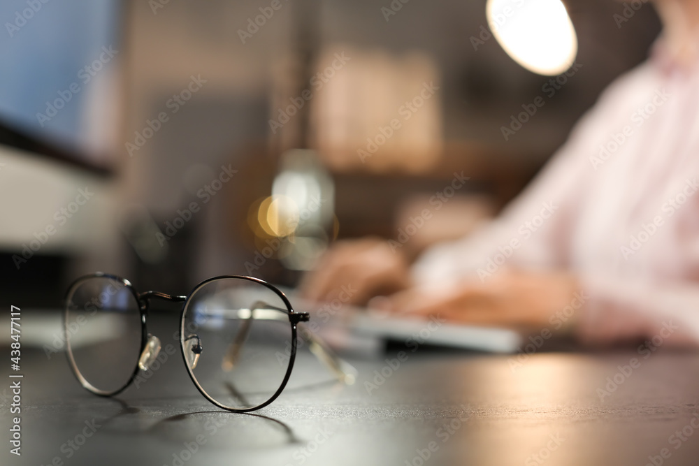 Stylish eyeglasses on table of working woman late in evening