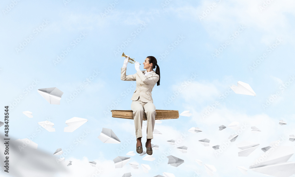 Young woman playing trumpet and sitting on book