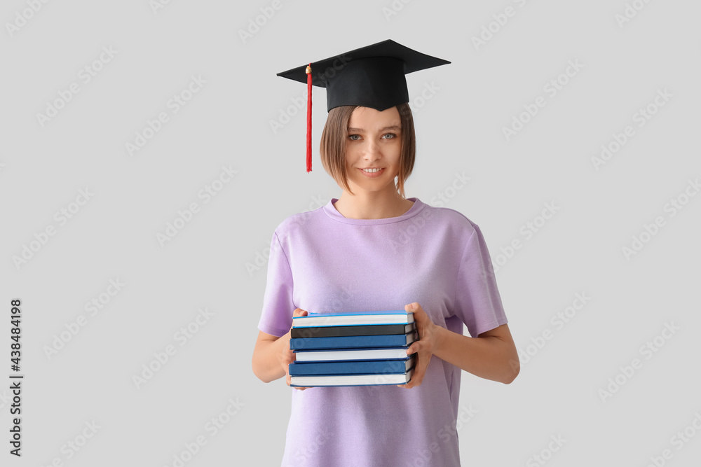 Female graduating student with books on light background