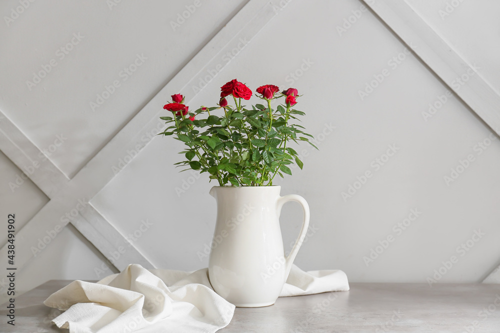 Beautiful red roses in pot on table near light wall