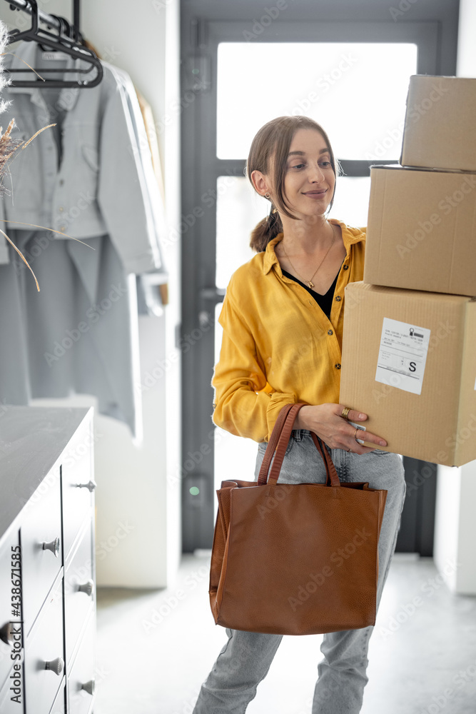 Young woman comes home with a parcels, holding three cardboard boxes in the hallway. Concept of buyi