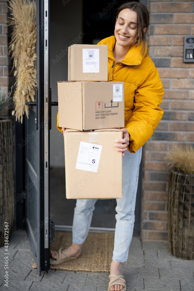 Housewife receiving goods purchased online on the porch of her house, holding cardboard boxes at the