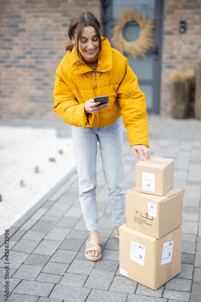 Woman receiving goods in front of her home, checking online purchases with a smart phone. Concept of