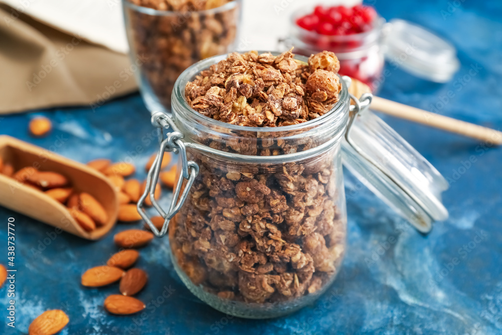 Glass jar with tasty granola on color background