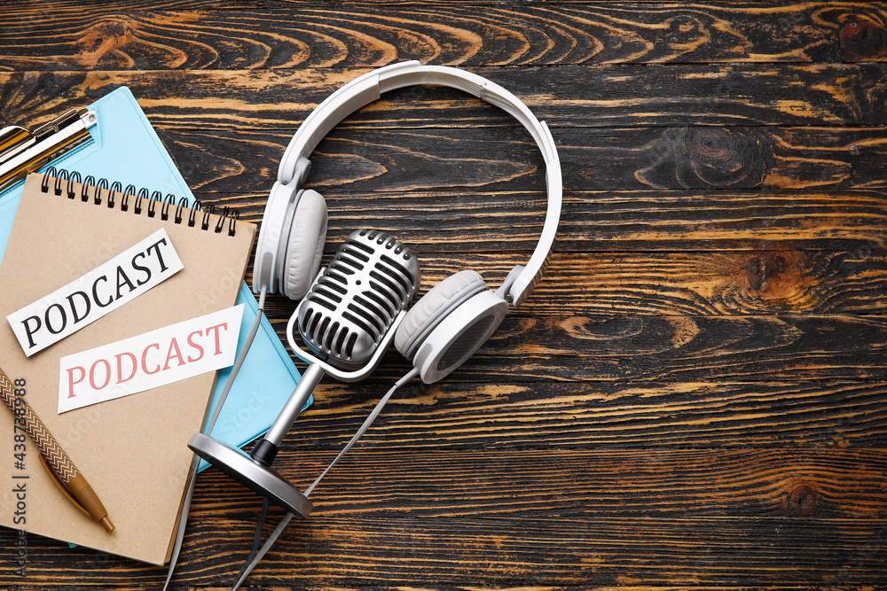 Retro microphone, headphones and notebooks  with word PODCAST on wooden background