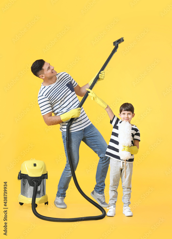 Father and son with vacuum cleaner on color background