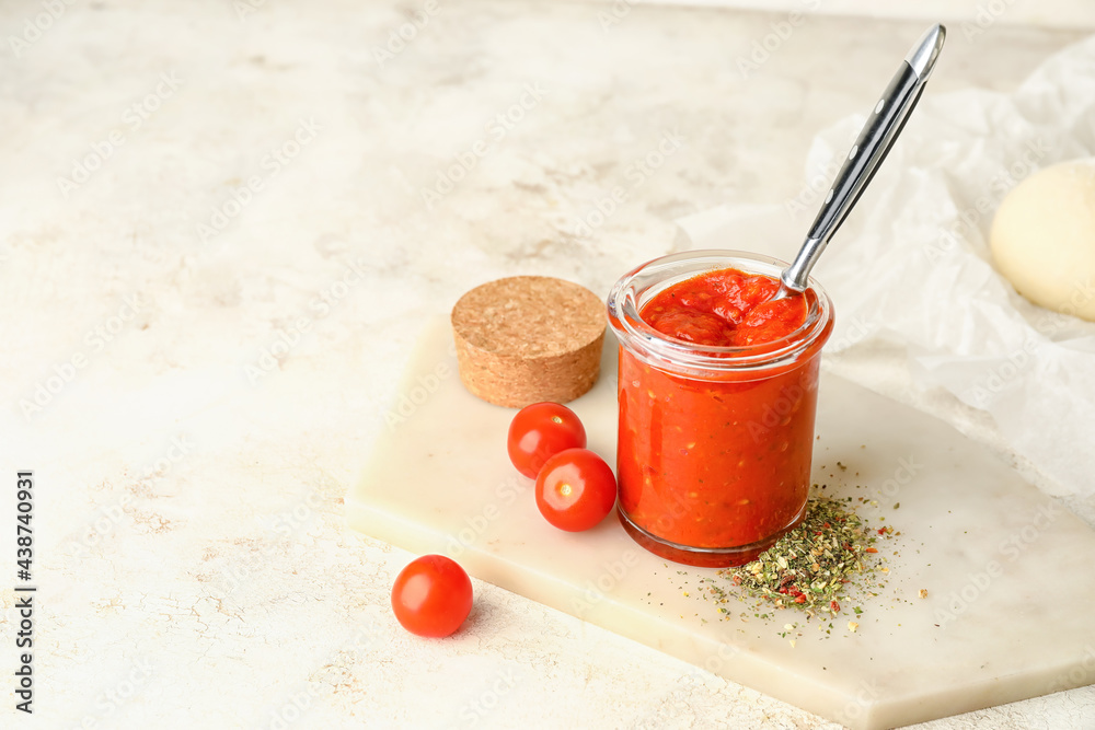 Board with glass jar of tasty sauce on light background