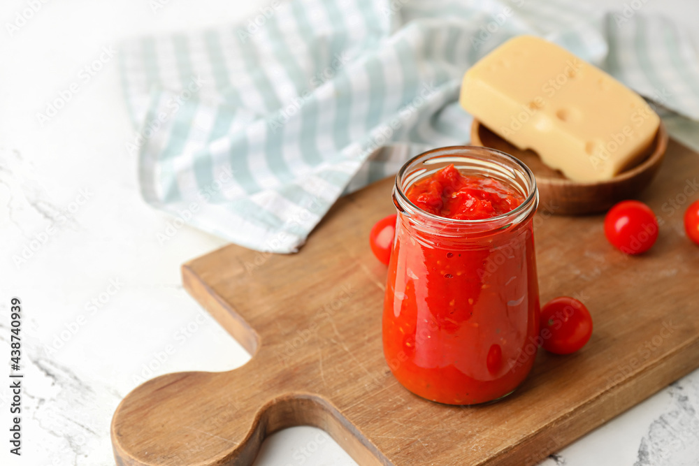 Board with glass jar of tasty sauce and cheese on light background, closeup