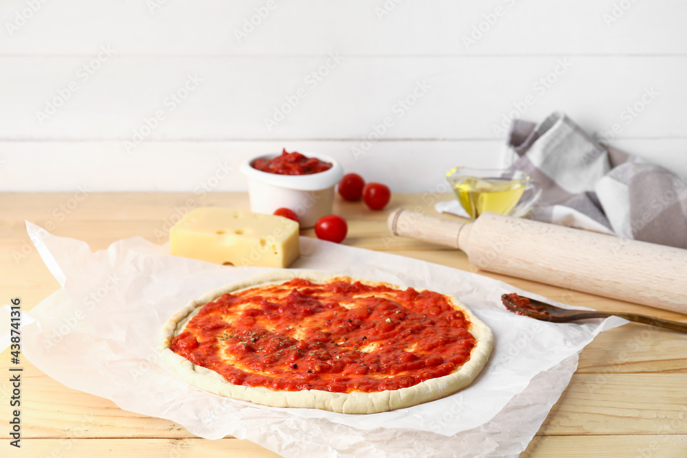 Pizza dough with tasty tomato sauce and cheese on wooden background