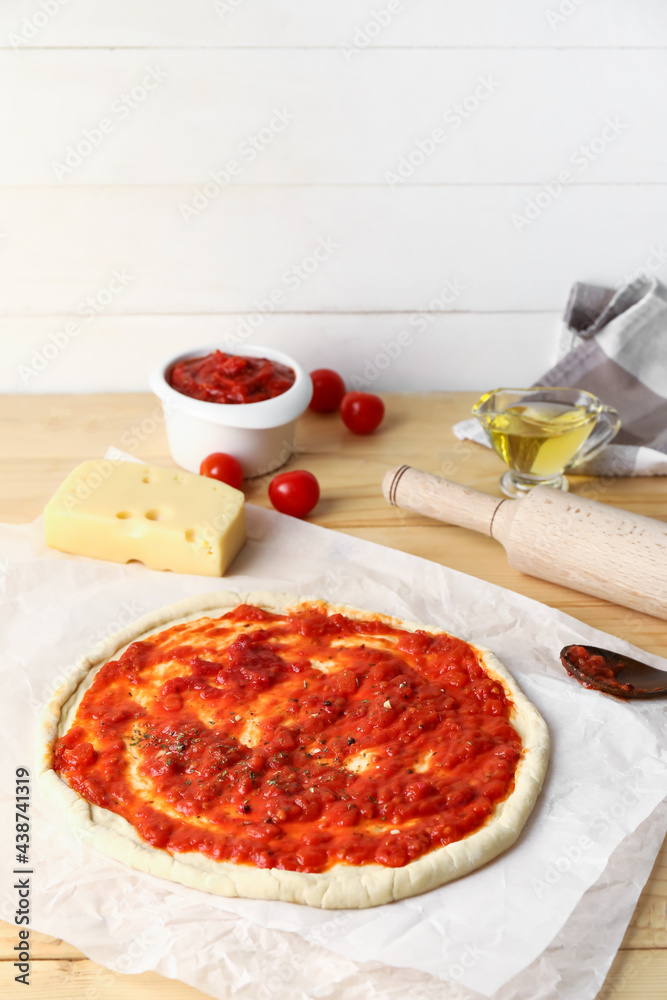 Pizza dough with tasty tomato sauce and cheese on wooden background