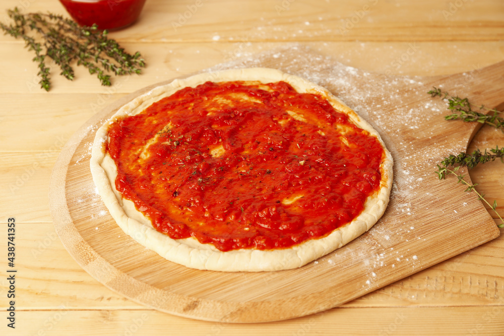 Pizza dough with tasty tomato sauce on wooden background