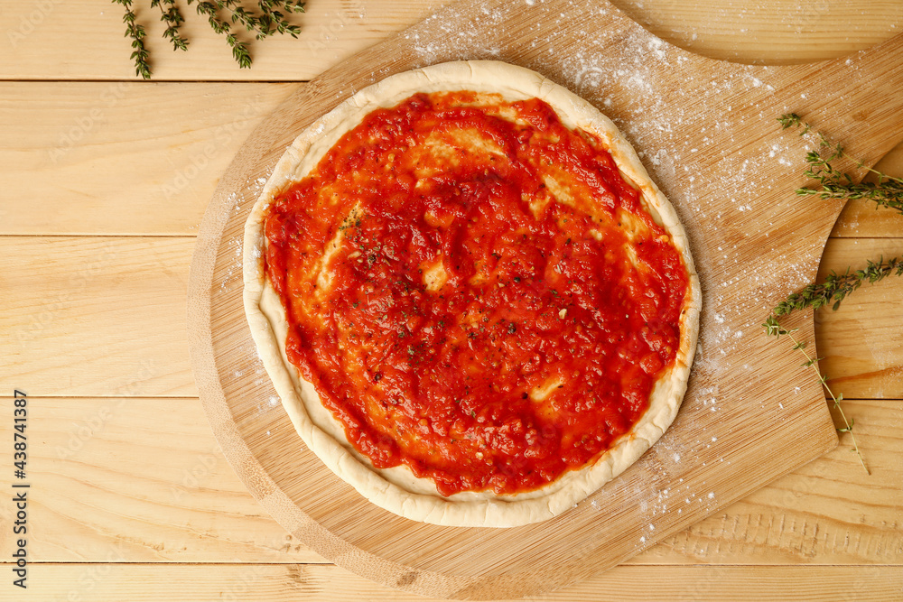 Pizza dough with tasty tomato sauce on wooden background