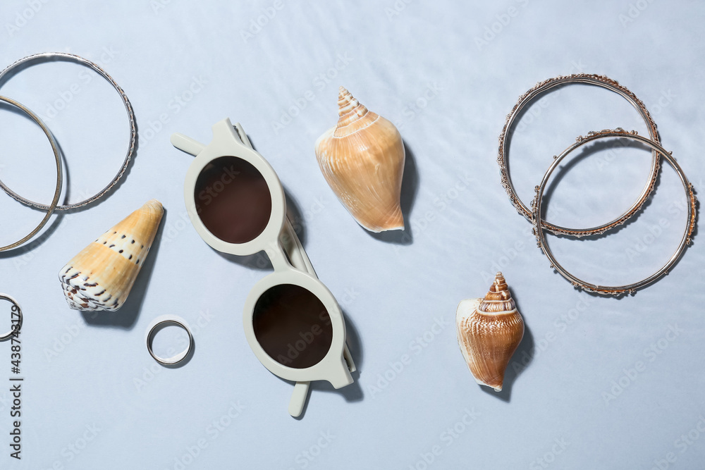 Sunglasses, accessories and seashells into water on grey background