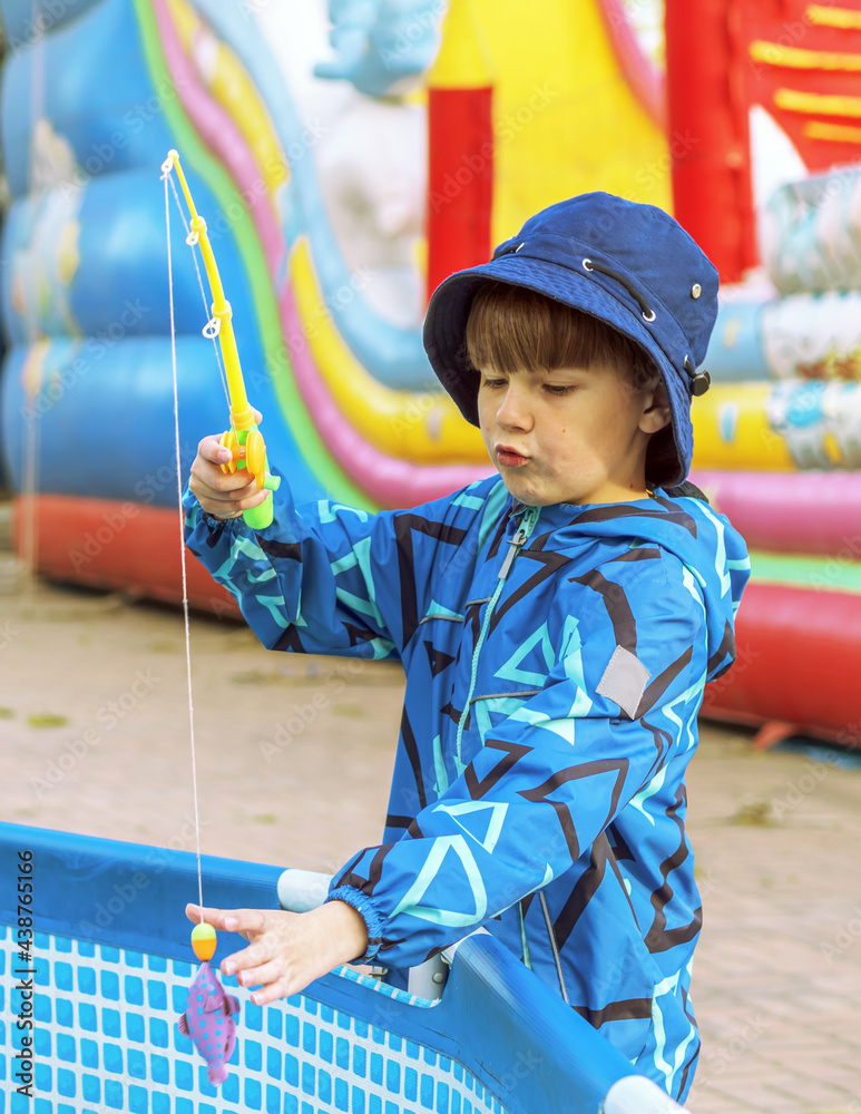 8 year old boy outdoors is fishing in the paddling pool.