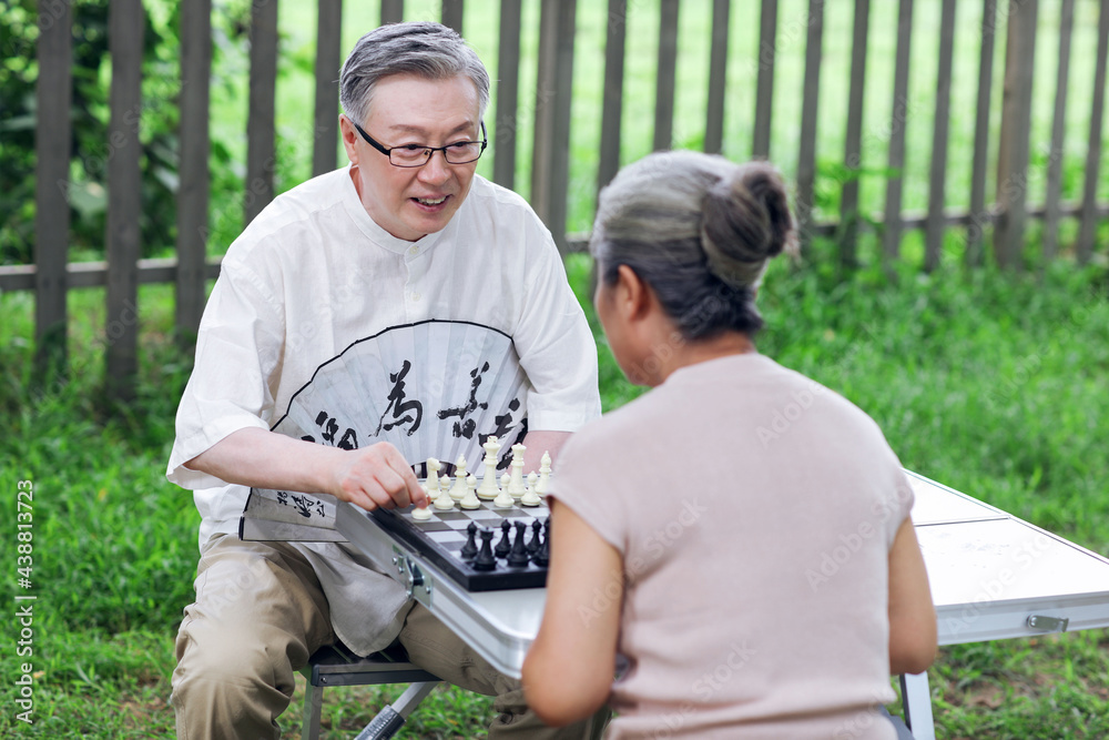 Happy old couple playing chess in the park