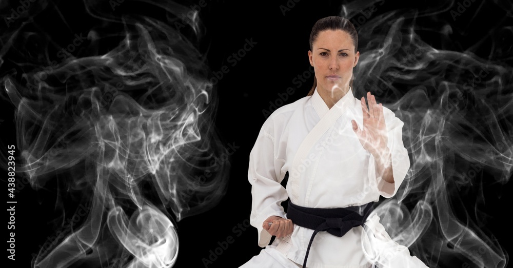 Composition of female martial artist over trails of smoke on black background