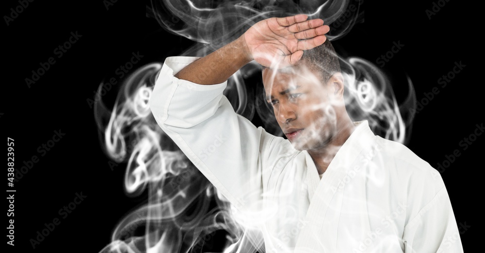 Composition of male martial artist over trails of smoke on black background