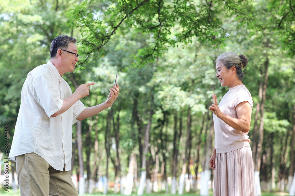 Happy old couple taking photos with mobile phone in the park