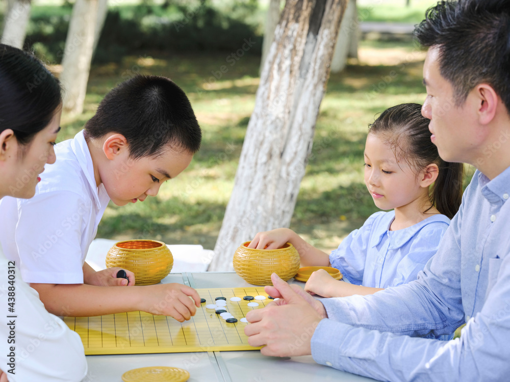 Happy family of four playing chess in the park