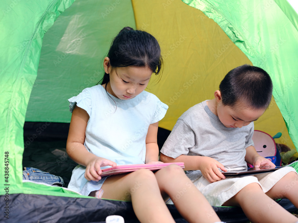 Two kids playing with tablets in the tent