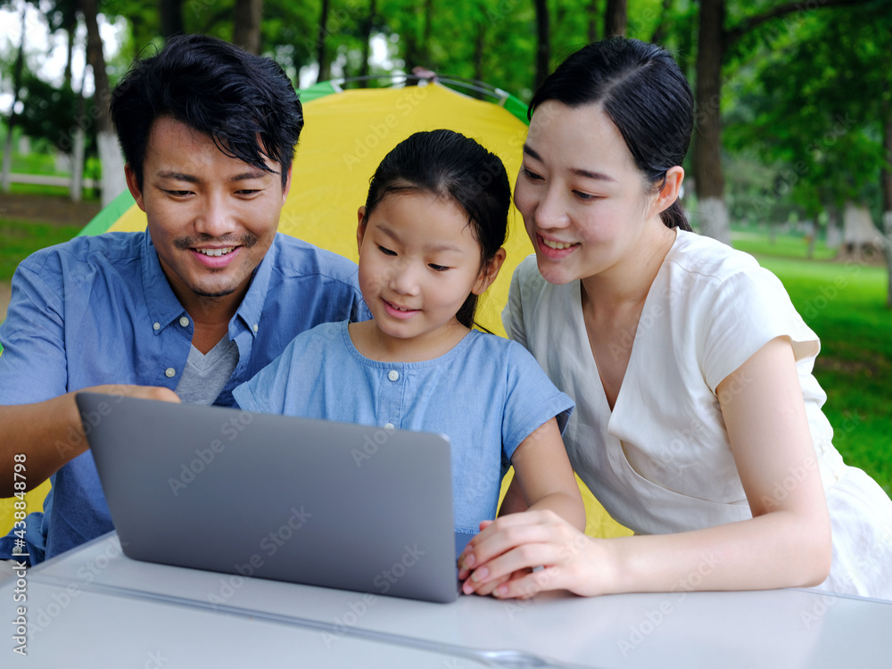 Happy family of three use computer to surf the Internet outdoors