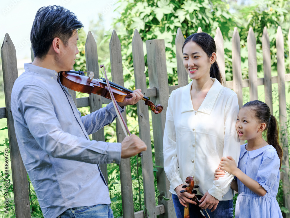 Happy family of three playing violin in the park