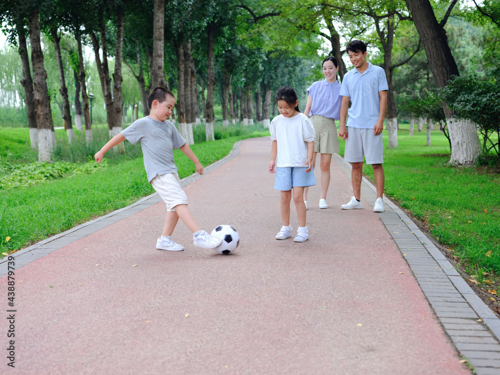 Happy family of four playing football in the park