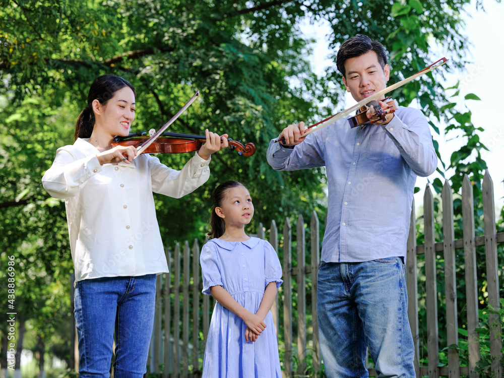 Happy family of three playing violin in the park