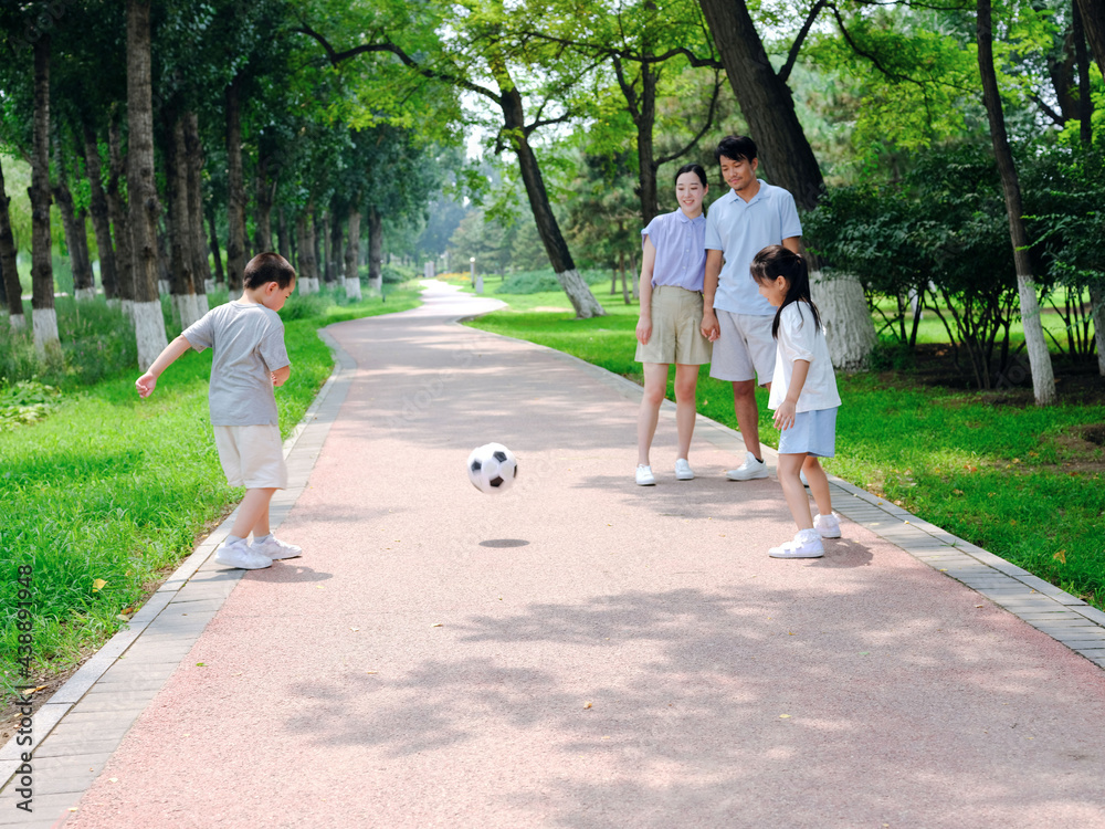 Happy family of four playing football in the park