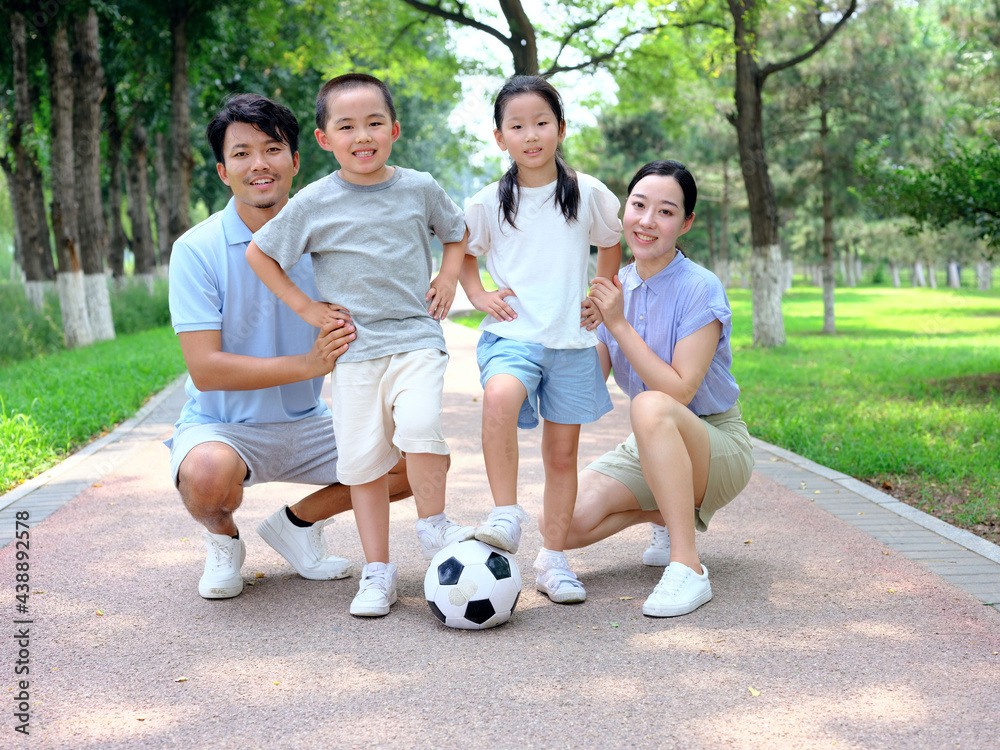 Happy family of four playing football in the park