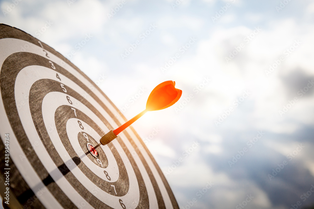 Close up shot red darts arrows in the target  of dartboard center on dark blue sky background. Busin