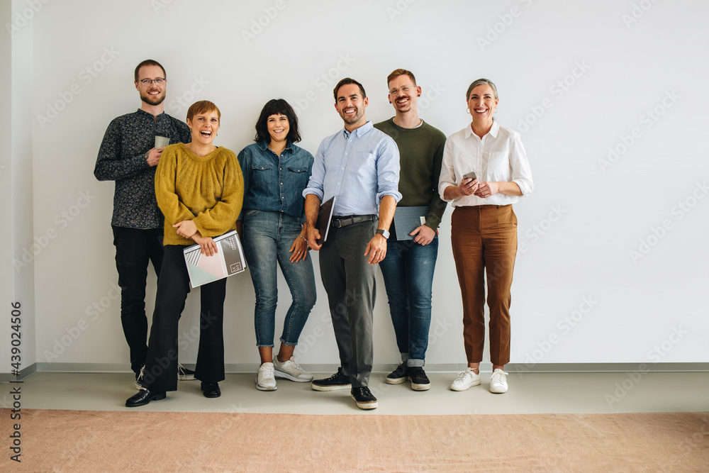 Happy colleagues standing against wall in office