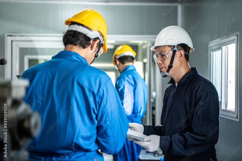 Asian male engineer explaining job to mechanical worker in workshop.	