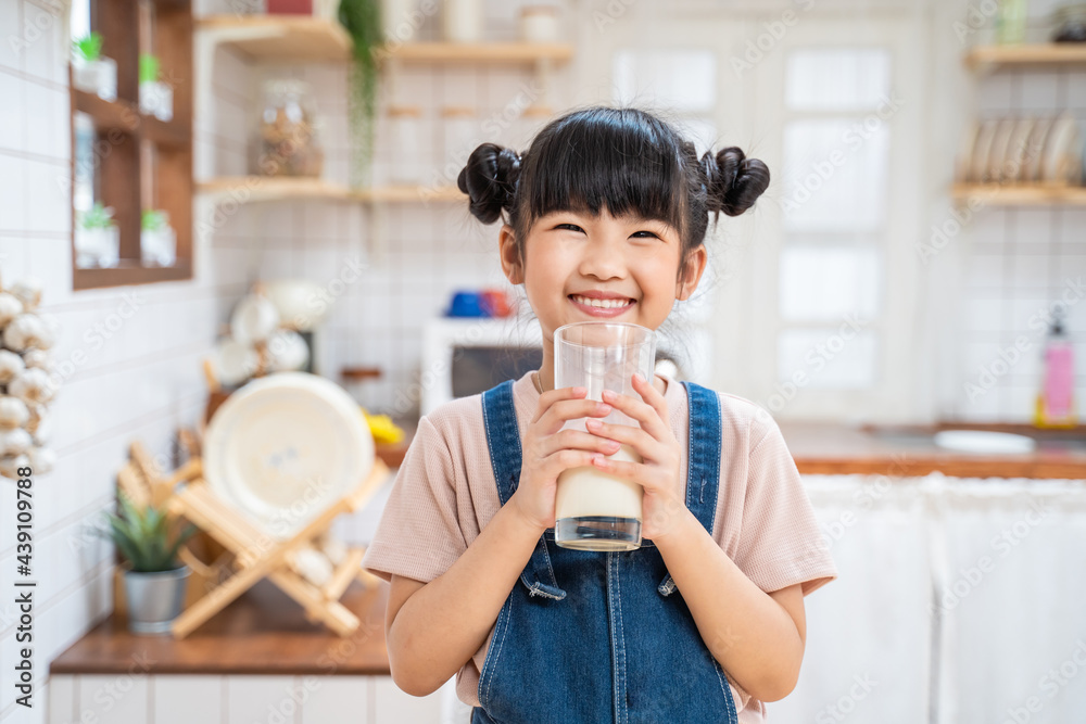 Asian little kid hold milk cup and look at camera in kitchen at home.