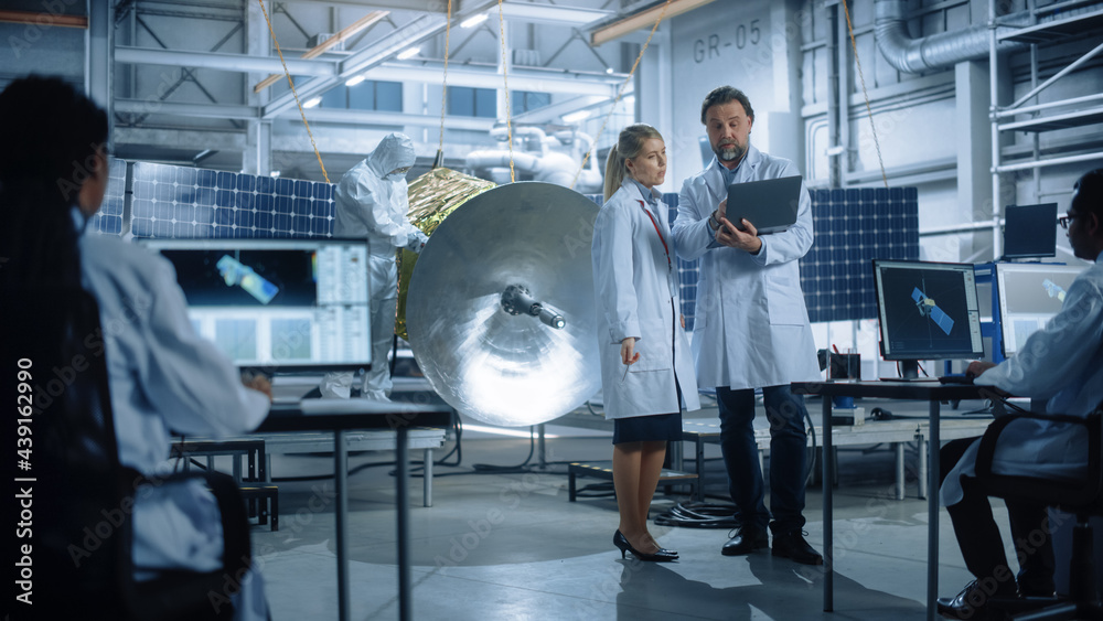 Engineer and Technician Talk, Use Laptop Computer while Working on Satellite Construction. Aerospace