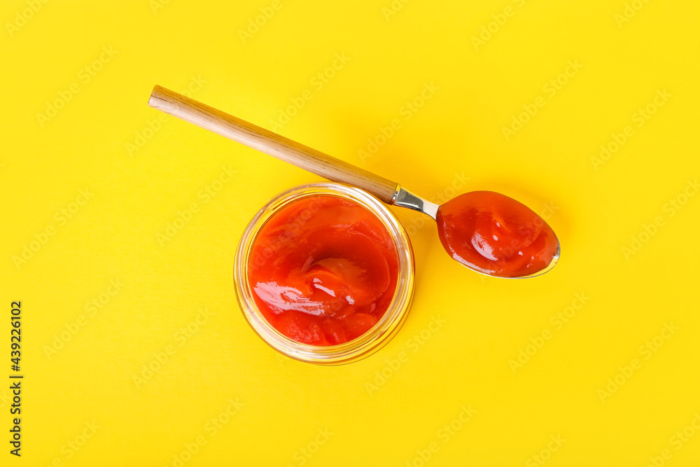 Jar and spoon with tasty ketchup on color background