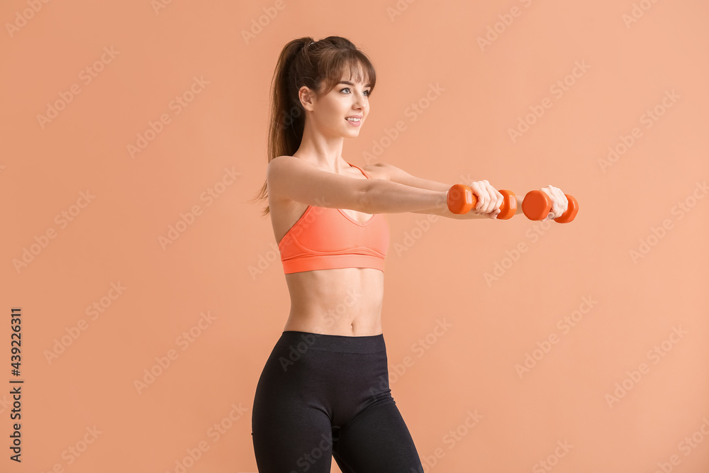 Sporty young woman training with dumbbells on color background