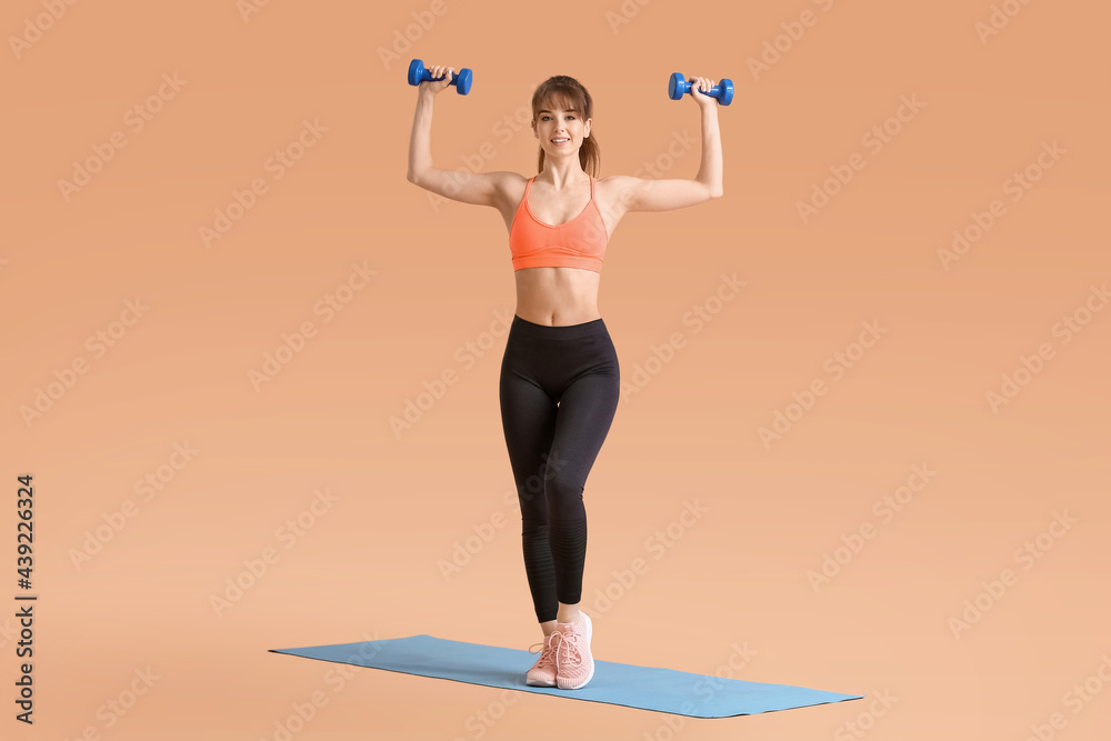 Sporty young woman training with dumbbells on color background