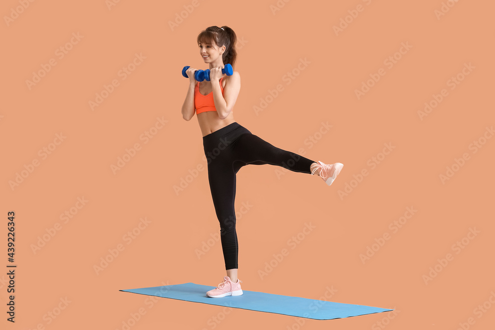 Sporty young woman training with dumbbells on color background