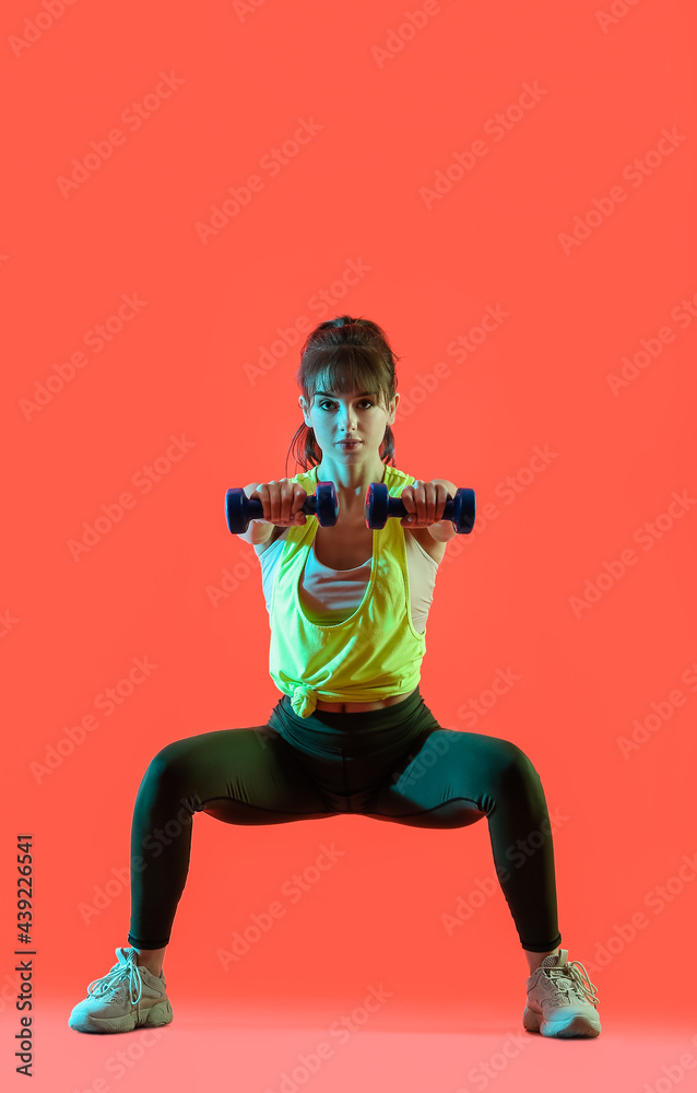 Sporty young woman training with dumbbells on color background