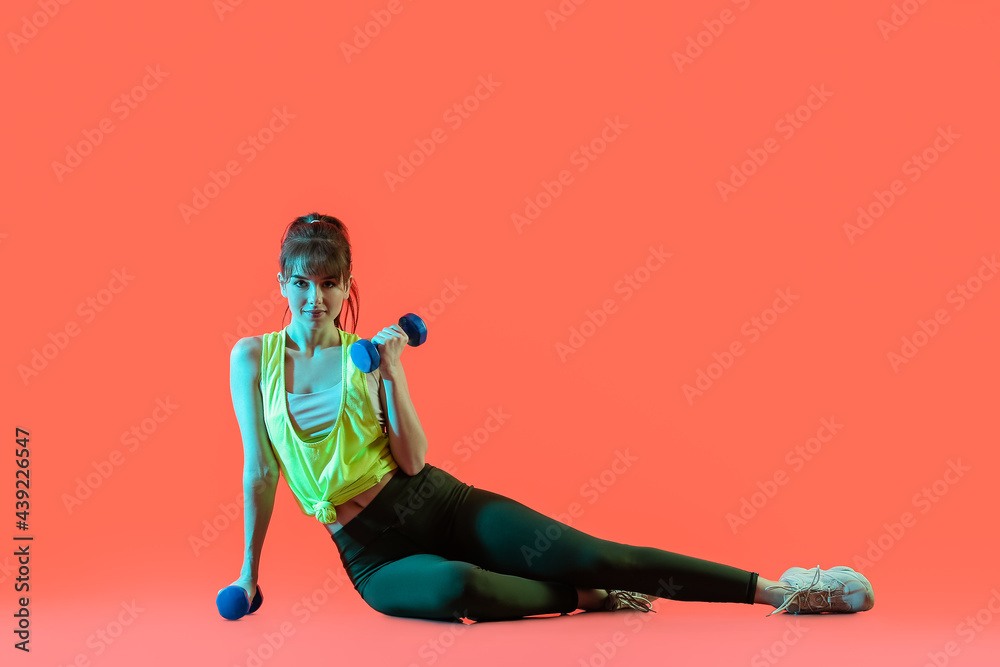 Sporty young woman with dumbbells on color background