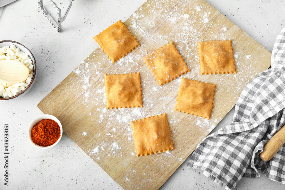 Wooden board with raw ravioli on table