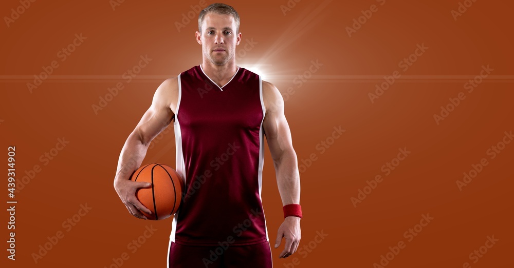 Portrait of caucasian male basketball player holding basketball against spot of light in background