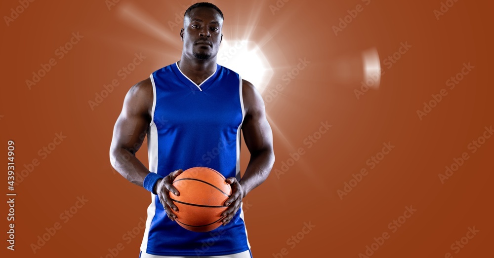 African american male basketball player holding basketball against spot of light in background