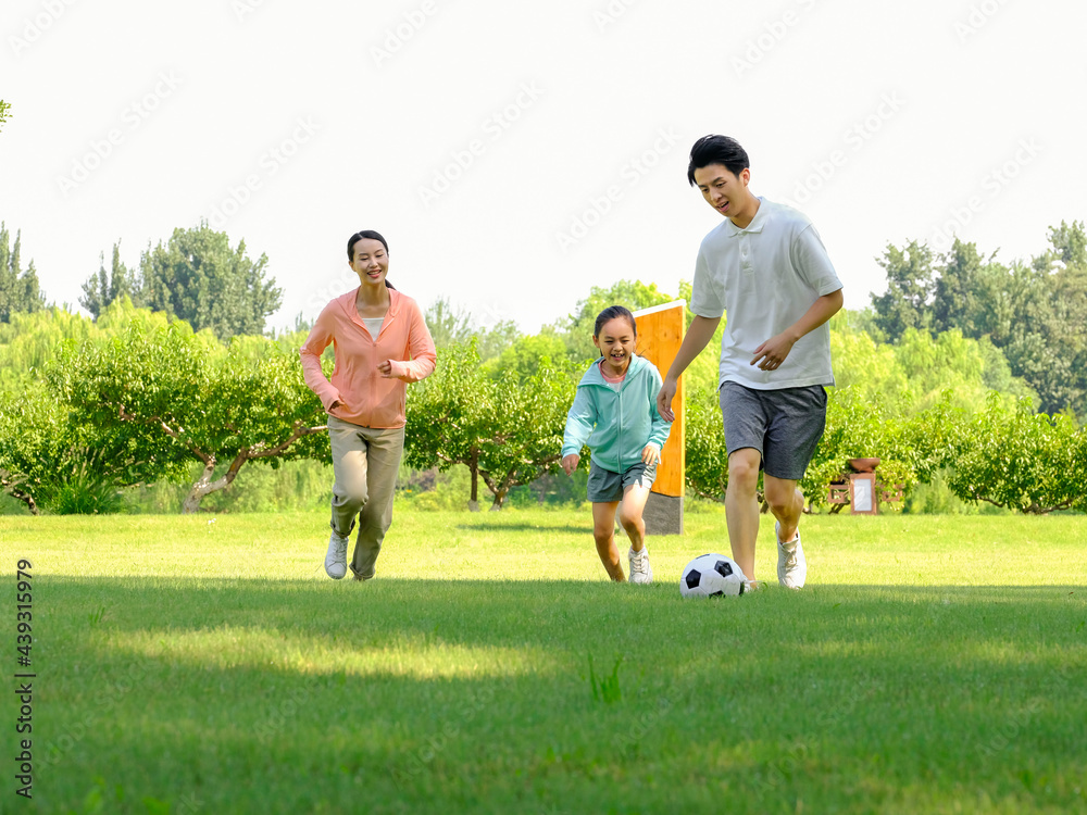 Happy family of three playing football in the park